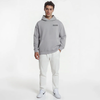 Homme en sweat gris clair TOURISMO, pantalon blanc et sneakers Nike sur fond blanc