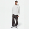 Homme portant un hoodie blanc TOURISMO avec un pantalon large foncé et des sneakers