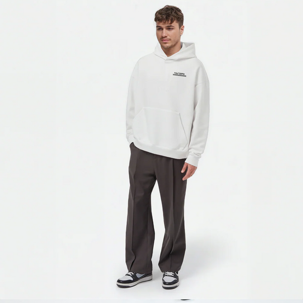 Homme portant un hoodie blanc TOURISMO avec un pantalon large foncé et des sneakers