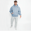 Homme portant un hoodie bleu clair TOURISMO avec jean clair, fond blanc