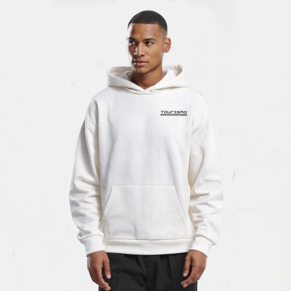 Sweat à capuche blanc pour homme, modèle "Grille Blanche" de Tourismo Clothing. Hoodie sans cordon, coupe droite avec poche kangourou et capuche épaisse. Logo brodé noir sur la poitrine gauche avec motif damier évoquant une ligne de départ. Le mannequin est de face, regard tourné vers la droite, expression calme et concentrée. Fond blanc neutre, lumière diffuse qui met en valeur la texture douce et structurée du tissu. Vêtement streetwear haut de gamme, inspiré du monde de la course automobile et du style é