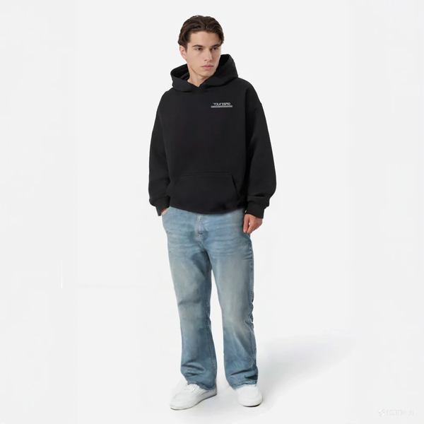 Homme en hoodie noir TOURISMO avec jean clair et baskets blanches, regard vers la gauche