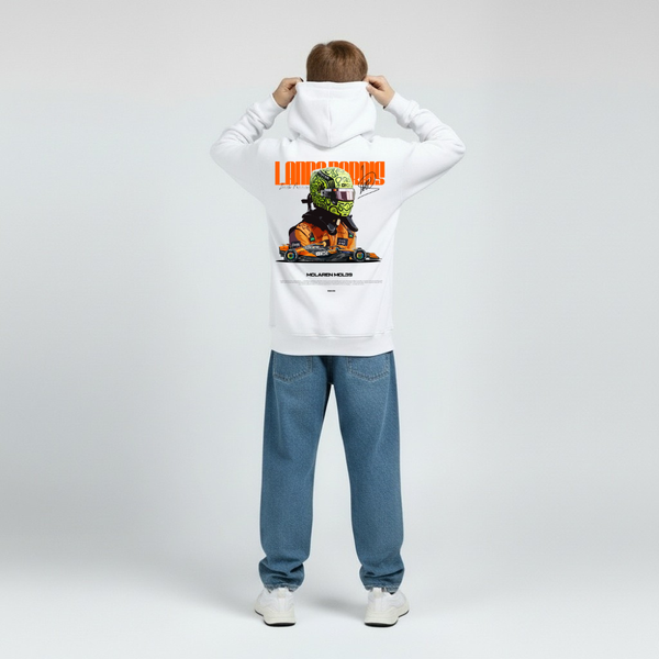Enfant vu de dos portant un sweat à capuche blanc Lando Norris, visuel graphique grand format sur le dos représentant le casque du pilote et la monoplace McLaren sur fond orange vif. Capuche relevée, jeans droits bleus, posture droite, fond studio gris clair neutre.