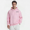 Homme en hoodie rose clair TOURISMO et pantalon blanc sur fond blanc
